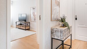 A hallway with a wooden floor, a TV on a wooden stand, and a console table with a plant. - GuestReady - Geometric Dawn in Vila do Conde (Vila do Conde)