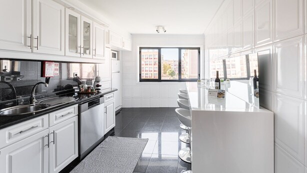 A modern kitchen with white cabinets, a black countertop, and a large window offering a city view. - GuestReady - Geometric Dawn in Vila do Conde (Vila do Conde)