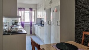 A modern kitchen with white cabinets, a stainless steel refrigerator, and a dining area with a wooden table and chairs.