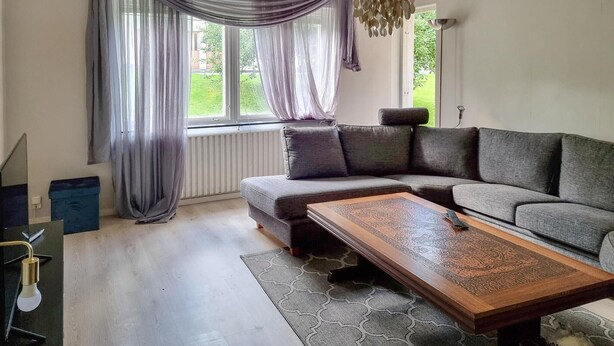 A modern living room with a sectional sofa, a wooden coffee table, and a large window with sheer curtains.