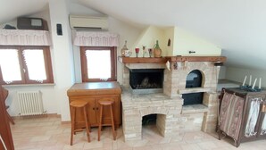 A cozy kitchen with a stone fireplace, wooden bar stools, and a window with a decorative valance. - Cosy apartment for 4 guests with A/C, WIFI, TV and panoramic view, close to Porto Recanati (Campanari)