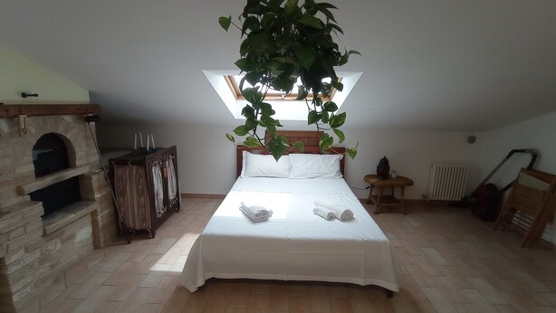 A bedroom with a bed, a wooden chest, a fireplace, and a hanging plant. - Cosy apartment for 4 guests with A/C, WIFI, TV and panoramic view, close to Porto Recanati (Campanari)