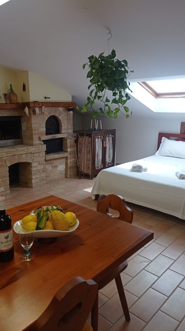 Cozy retreat with a stone fireplace, dining table, and comfortable bed, complete with a skylight and lush greenery.