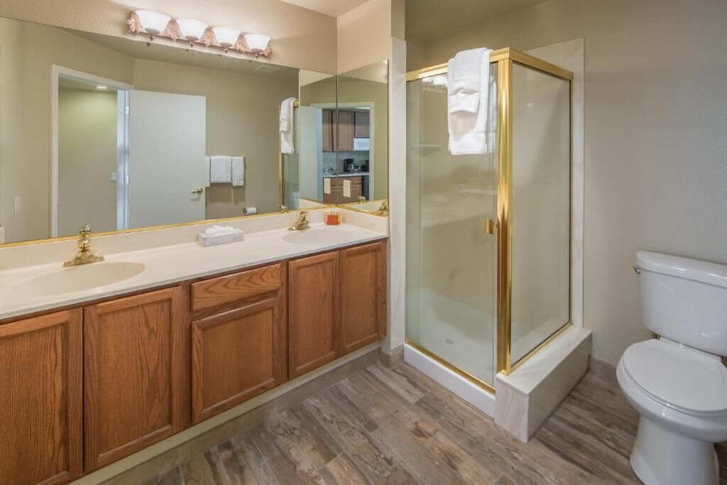 A bathroom with a wooden vanity, a large mirror, a glass shower enclosure, and a white toilet.
