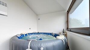 A small, private spa room with a hot tub, a window, and a wall-mounted air conditioner.