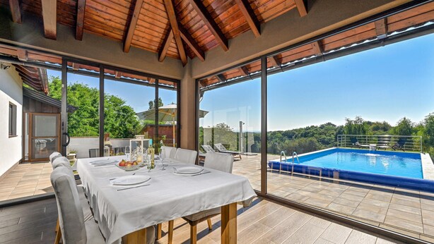 A dining area with a table set for four, overlooking a swimming pool and lush greenery.