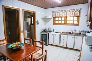 Una cocina con gabinetes blancos, una estufa y un ventanal con cortina a cuadros.