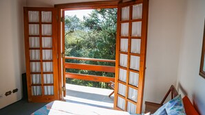 Un dormitorio con cama, un banco de madera y un balcón con vista a árboles.