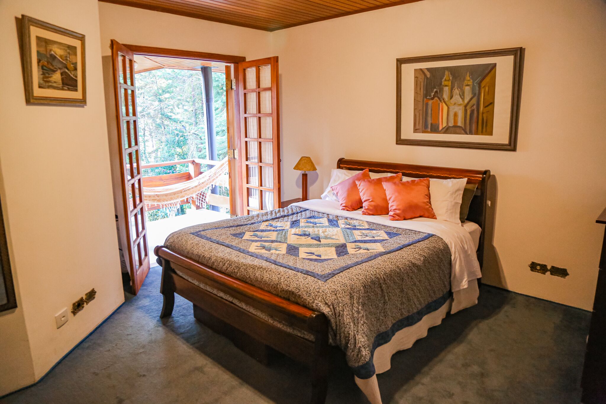 A bedroom with a wooden bed, a quilt, and a hammock outside the door.