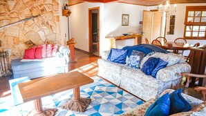 Una sala de estar acogedora con una pared de piedra, techo de madera, sofá estampado y comedor con mobiliario de madera.