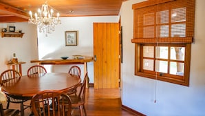 Un comedor con mesa y sillas de madera, una araña y un ventanal con persianas.