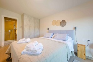 Quarto de hotel com uma cama, chuveiro e luminária fixada na parede.