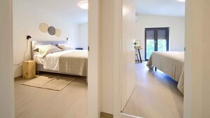 A bedroom with two beds, a bedside table, a lamp, and a window with blinds.