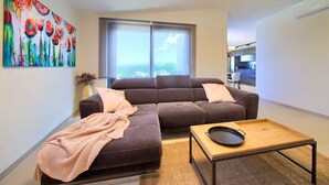A modern living room with a brown sofa, a small wooden table with a pan, and a colorful abstract painting on the wall.