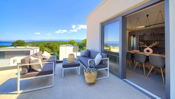 A modern outdoor balcony with a sofa, chairs, and a dining table.