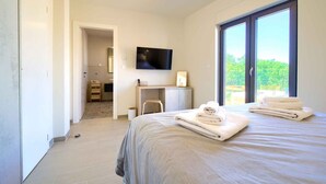 A modern hotel room with a large bed, a desk, a TV, and a balcony with a view.