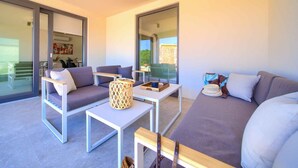 A modern living room with a grey sofa, two armchairs, a coffee table, and a small side table. Large windows provide a view of the outside.