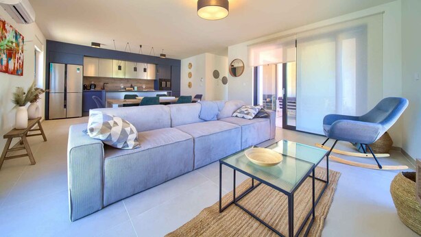 A modern living room with a sofa, a glass coffee table, and a blue armchair.