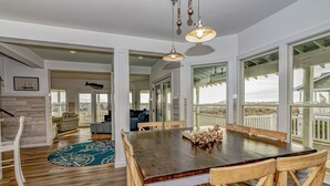 A spacious dining area with a large wooden table and chairs, a blue patterned rug, and large windows offering views of the outdoors. - Ocean front home, access to both clubs and large porches! Breaking Point (Bald Head Island)