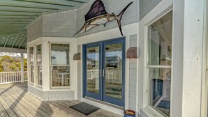 A covered porch with a wooden deck, a blue door, and a large fish mounted above the door. - Ocean front home, access to both clubs and large porches! Breaking Point (Bald Head Island)