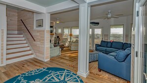 A spacious living area with a staircase, a blue sofa, and a view of the outdoors. - Ocean front home, access to both clubs and large porches! Breaking Point (Bald Head Island)