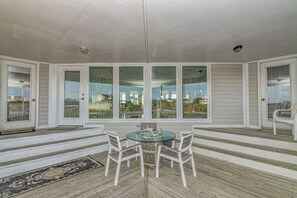 A covered patio with a glass table and white chairs, large windows, and a view of a house.