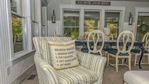 A cozy room with striped armchairs, a dining table with chairs, and a sign above the table reading "EAT, DRINK, AND BE MERRY".