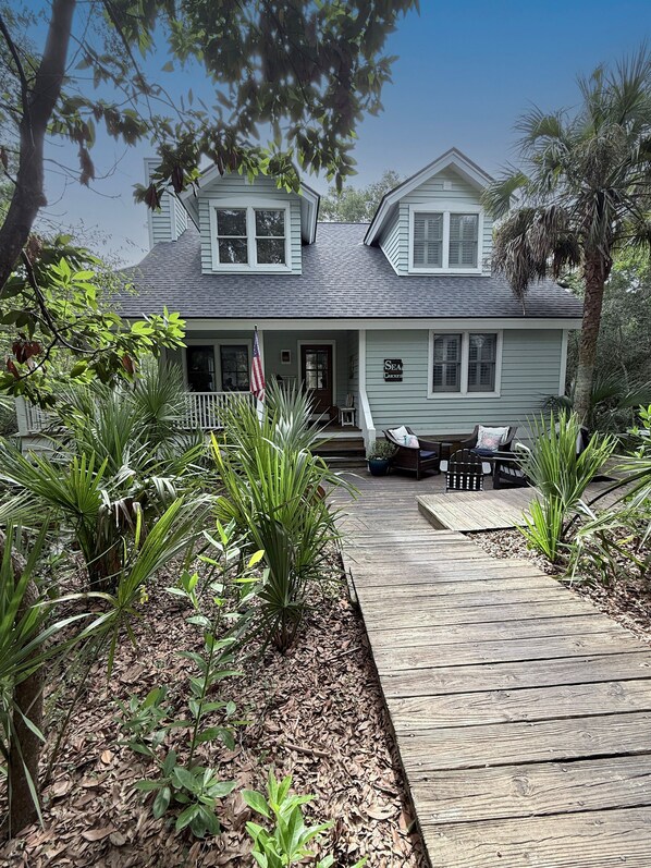 A two-story house with a porch, a flag, and a sign that reads 'Sea Cottage.'