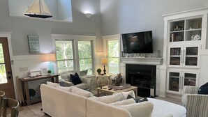 A spacious living room with a large white sofa, a fireplace, a television, and a bookshelf.