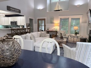A spacious living room with a large white sofa, a dining table, and a kitchen area with white cabinets.