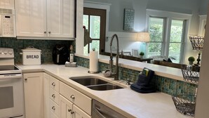 A modern kitchen with white cabinets, a stainless steel dishwasher, and a large window providing natural light.