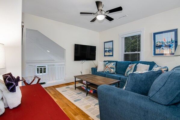A living room with a blue sofa, a wooden coffee table, a red table, and a ceiling fan.