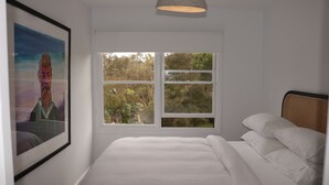 A bedroom with a large bed, a window with a view of trees, and a framed painting on the wall. - Coastal Retreat/ Holiday Home in Rye (Rye)