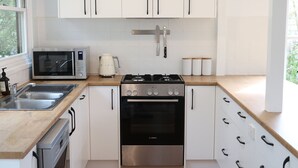 A modern kitchen with white cabinets, stainless steel appliances, and a wooden countertop. - Coastal Retreat/ Holiday Home in Rye (Rye)