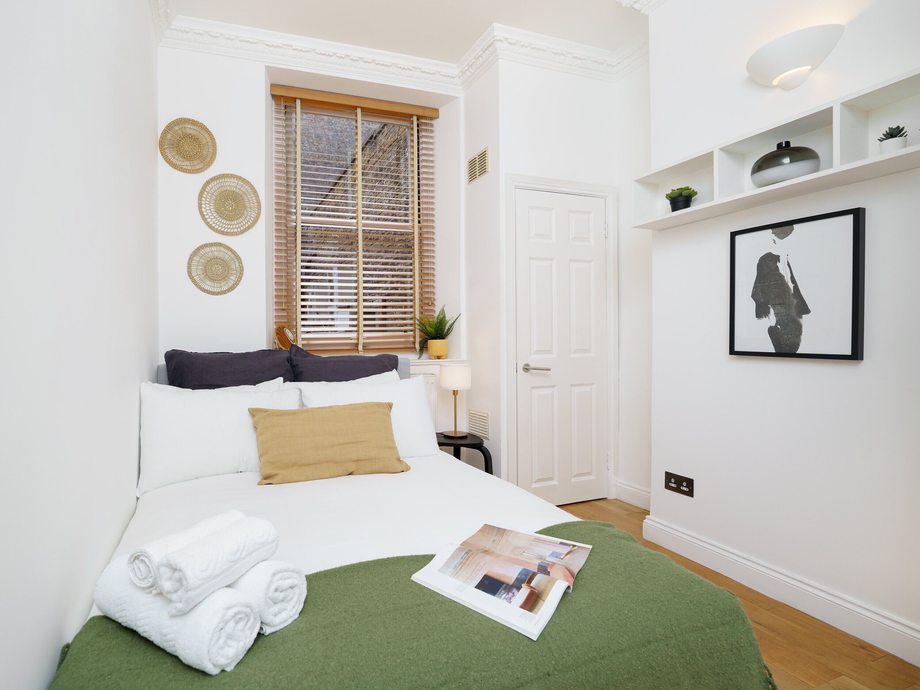 A neatly arranged bedroom with a bed, pillows, a green throw, and a magazine on the bed.