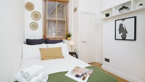 Een netjes opgemaakt slaapkamer met een bed, kussens, een groene plaid en een tijdschrift op het bed.