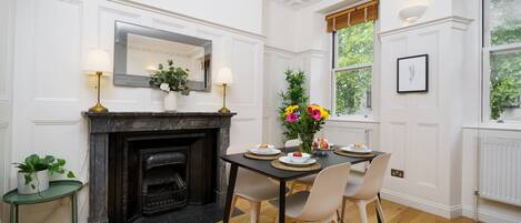 A dining area with a fireplace, white walls, and a window with a view of greenery.