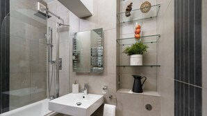 Een moderne badkamer met een douchecabine van glas, een witte wastafel en een glazen plank met decoratieve voorwerpen.