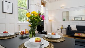 Een eettafel gedekt met borden, kommen en appels, een vaas met bloemen, en een moderne woonkamer op de achtergrond.