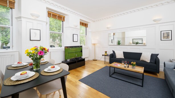 Een moderne woonkamer met een eethoek, een zwarte bank en een televisie.