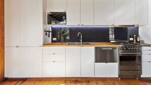 A modern kitchen with white cabinets, a wooden countertop, a stainless steel sink, and a built-in oven. - Charming off-grid cabin with room to explore (Briagolong)
