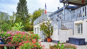 A house with a balcony, a flag, and a garden with various plants and flowers. - Nice apartment in Chambornay-Lès-Pin (Chambornay-Lès-Pin)