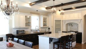A spacious kitchen with white cabinetry, a large island with bar stools, and a dining area with a wooden table and chairs. - Picturesque Rosemary Retreat (California)