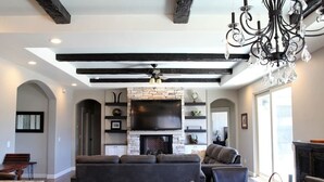 A modern living room with a fireplace, a large TV, and a chandelier. - Picturesque Rosemary Retreat (California)