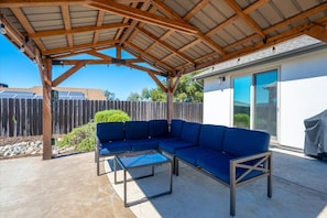 A covered patio area with a sectional sofa and a glass-top table.