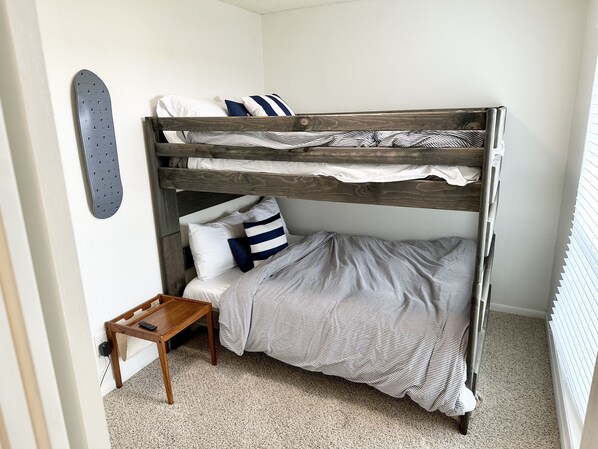 A bunk bed with a wooden frame, a small wooden table, and a striped bedspread. - Quiet West End Beach House • Beach & Bay Views • Walk to Beach (Galveston)