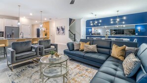 A modern living room with a blue sofa, grey armchairs, and a glass coffee table. - 5 Star Villa Regale – Royal Comfort and Grandeur (Orlando)