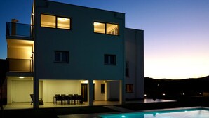 Una casa moderna de dos pisos con piscina, mobiliario exterior y amplias ventanas.