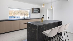 Cocina moderna con isla de mármol, taburetes de bar e iluminación colgante.