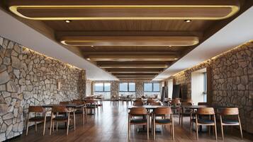 Un'ampia sala da pranzo con tavoli e sedie in legno, pareti in pietra e un soffitto alto con illuminazione a incasso.